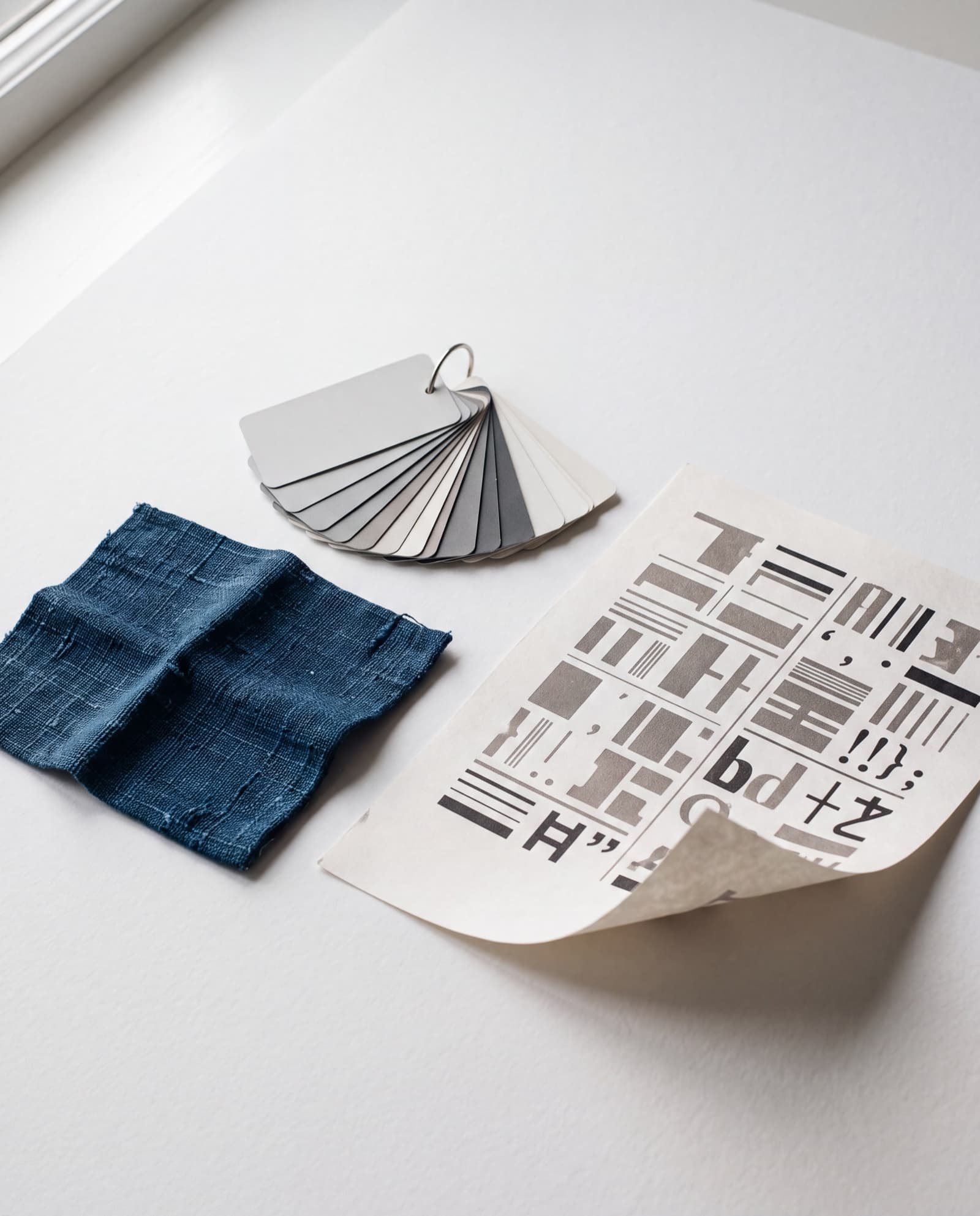 A still life of design samples — an indigo-dyed swatch, a fan of paint chips and a printed type specimen on paper.